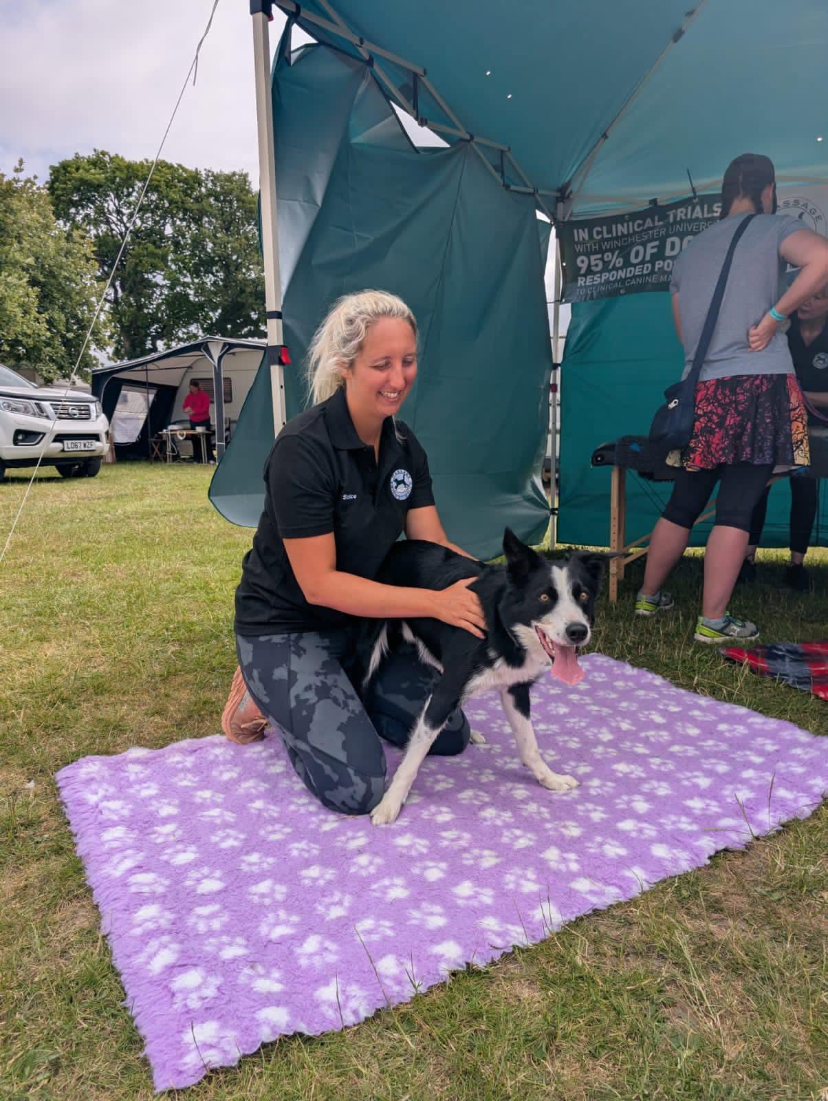 Shanice with a black and white collie on a purple blanket at an outdoor event
